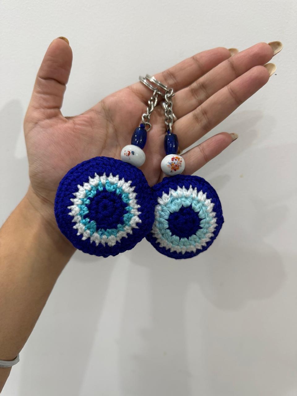 Two blue and white crochet evil eye keychains held in a hand