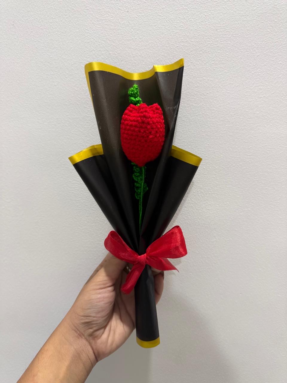 Single handmade crochet red rose wrapped in black paper with a red ribbon